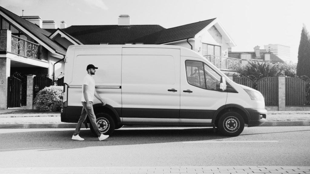 Monochrome photo of man walking in front of transport van
